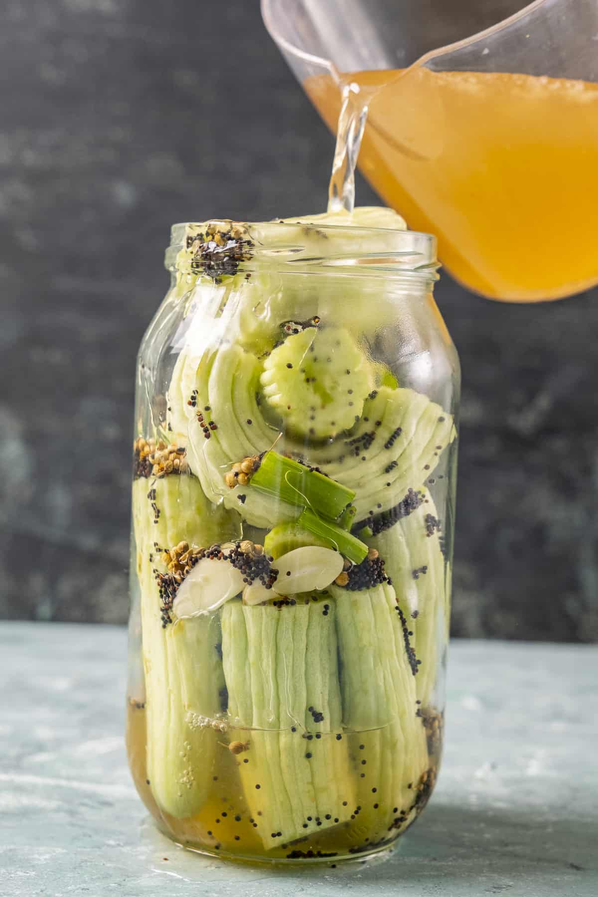 Pouring pickling brine into a jar filled with cucumbers.