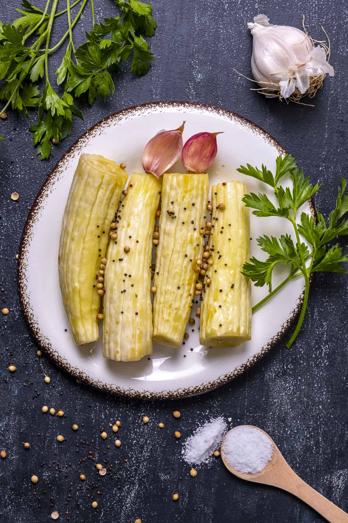 Pickled Armenian cucumbers on a white plate. Garlic cloves and parsley on the side.