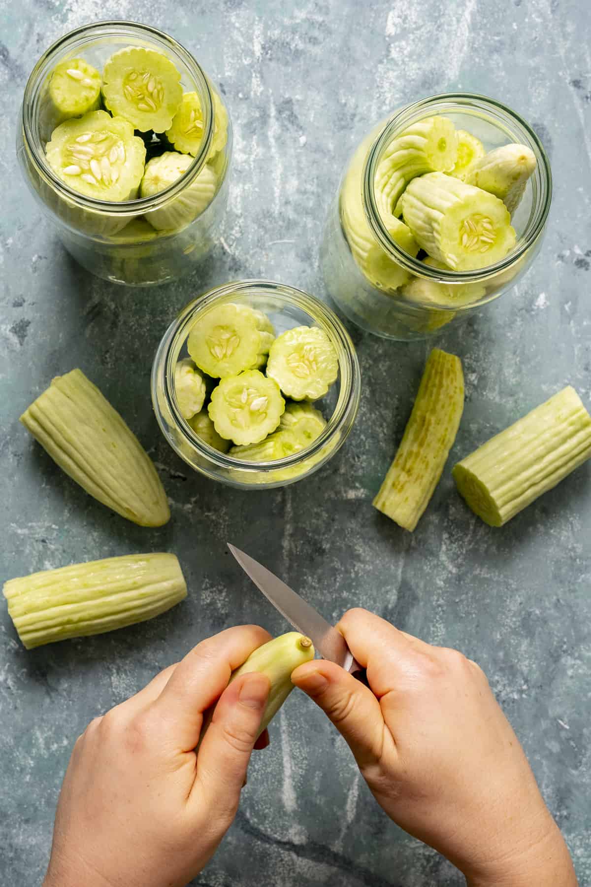 Hands cutting Armenian cucumbers and placing them into jars.