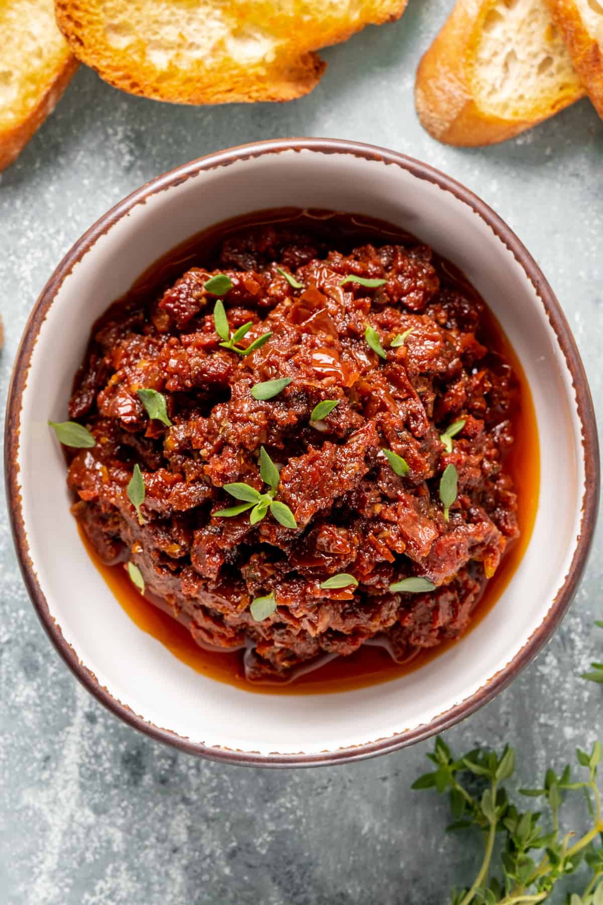 Sun-dried tomato sauce garnished with fresh thyme leaves in a white ceramic bowl.