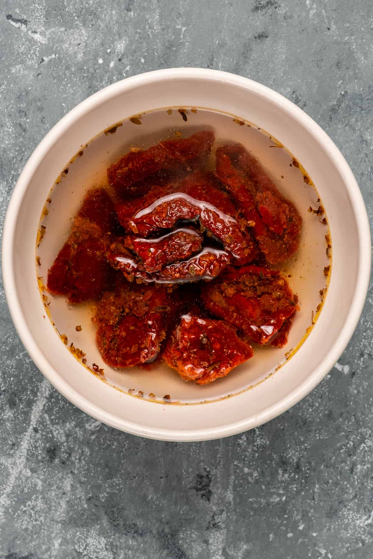 Sun-dried tomatoes soaked in water in a white bowl on a grey background.