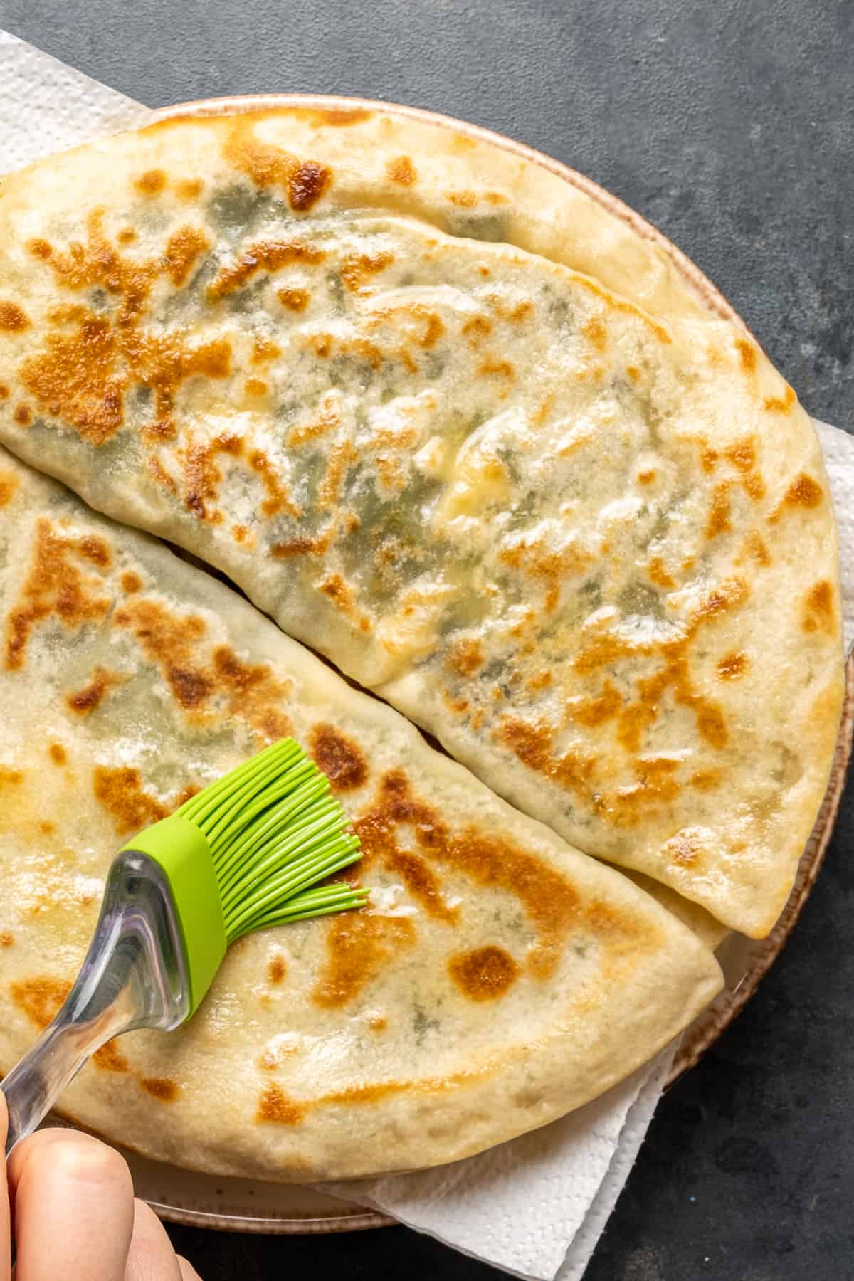 A green silicone brush spreading the cooked gözlemes with olive oil