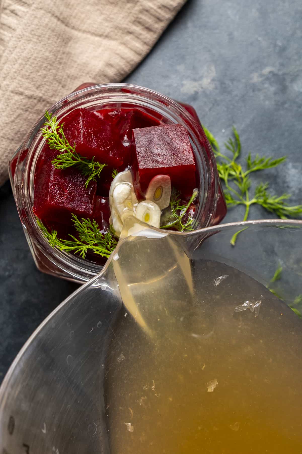 Pouring pickle brine over chopped beets in a jar.