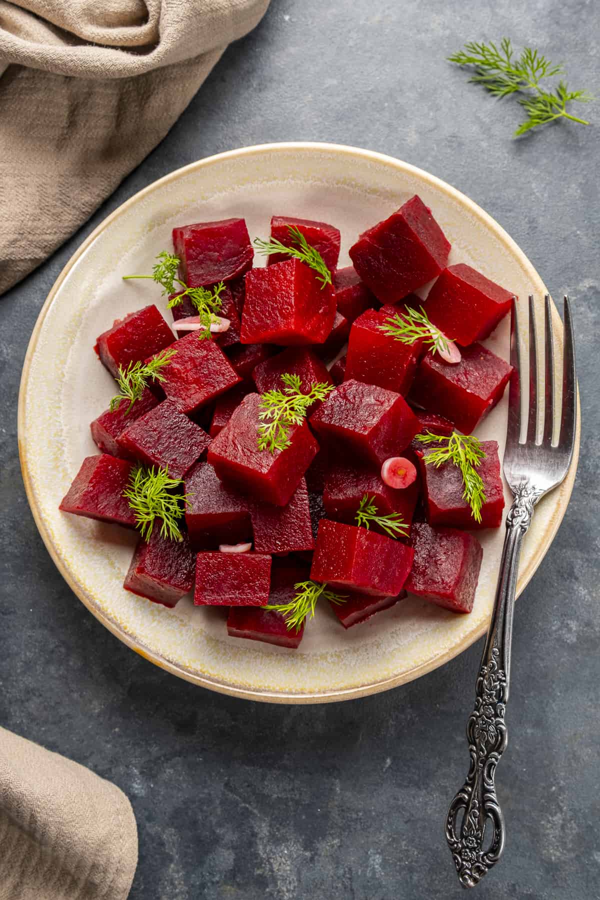 Pickled beets on a plate garnished with fresh dill.