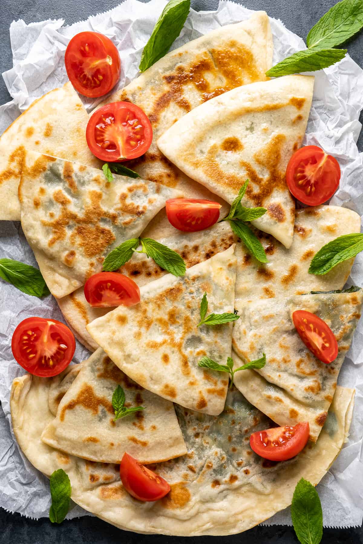 Gözleme sliced in triangles served with halved cherry tomatoes and fresh mint leaves.