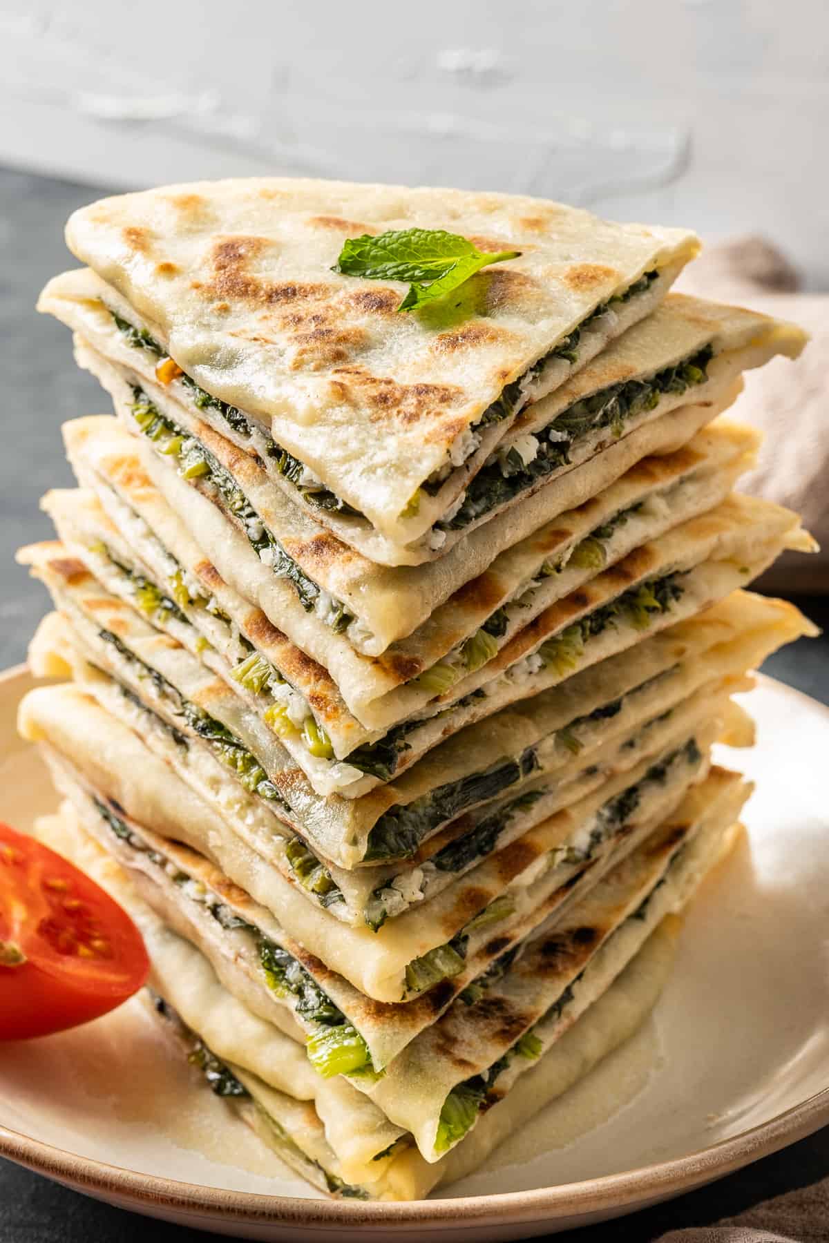 A stack of gozleme filled with spinach and cheese and a sprig of fresh mint on the top.