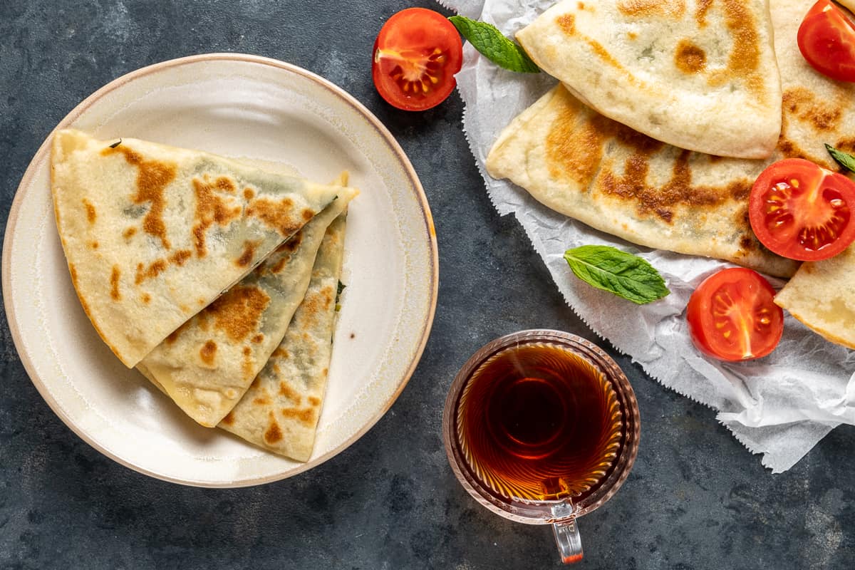 Gozleme slices on a plate and more on a larger plate accompanied by a glass cup of Turkish tea.