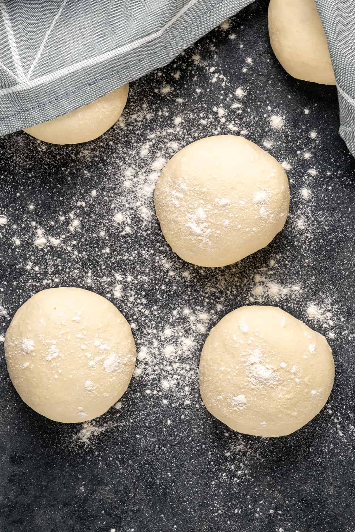 Dough patties half covered with a kitchen towel on a dark background.