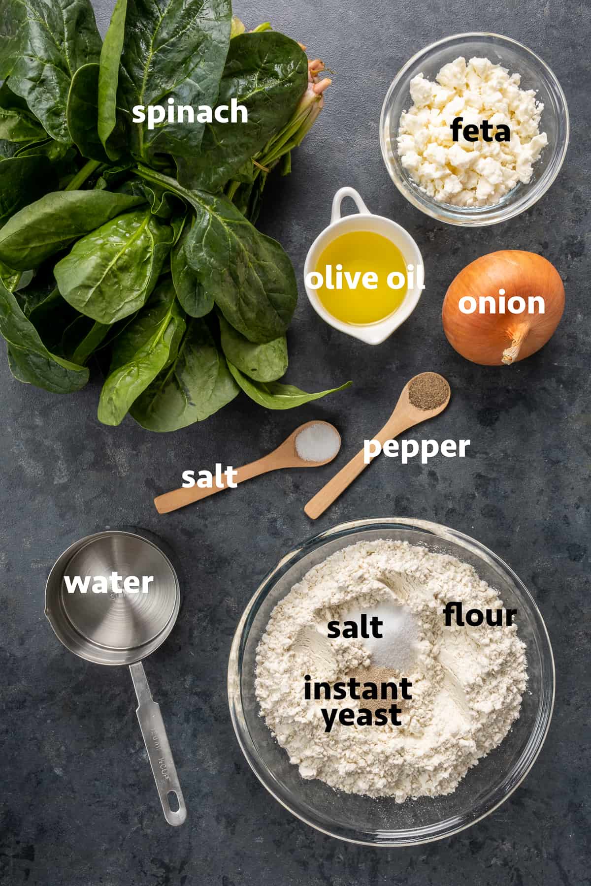 Gozleme dough ingredients in a bowl and spinach leaves, olive oil , onion, salt and pepper and cheese on a dark background.