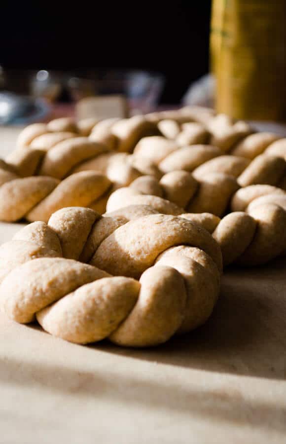 Braided ring shaped simit dough on brown baking sheet from front view, more on the back.