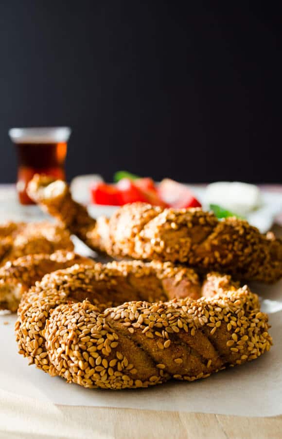 Whole wheat simits on a wooden board from front view, a glass of Turkish tea, tomatoes and cucumbers beking them.