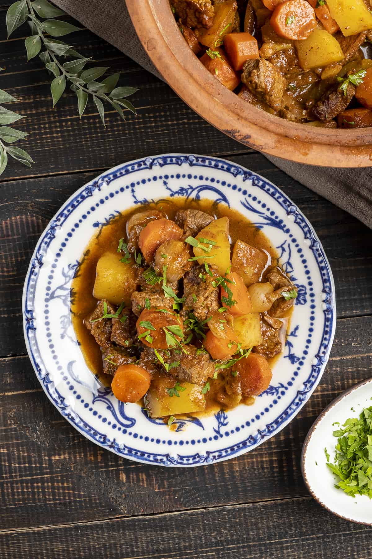 Beef and vegetable stew in a white and blue dish and a clay pot on the side.
