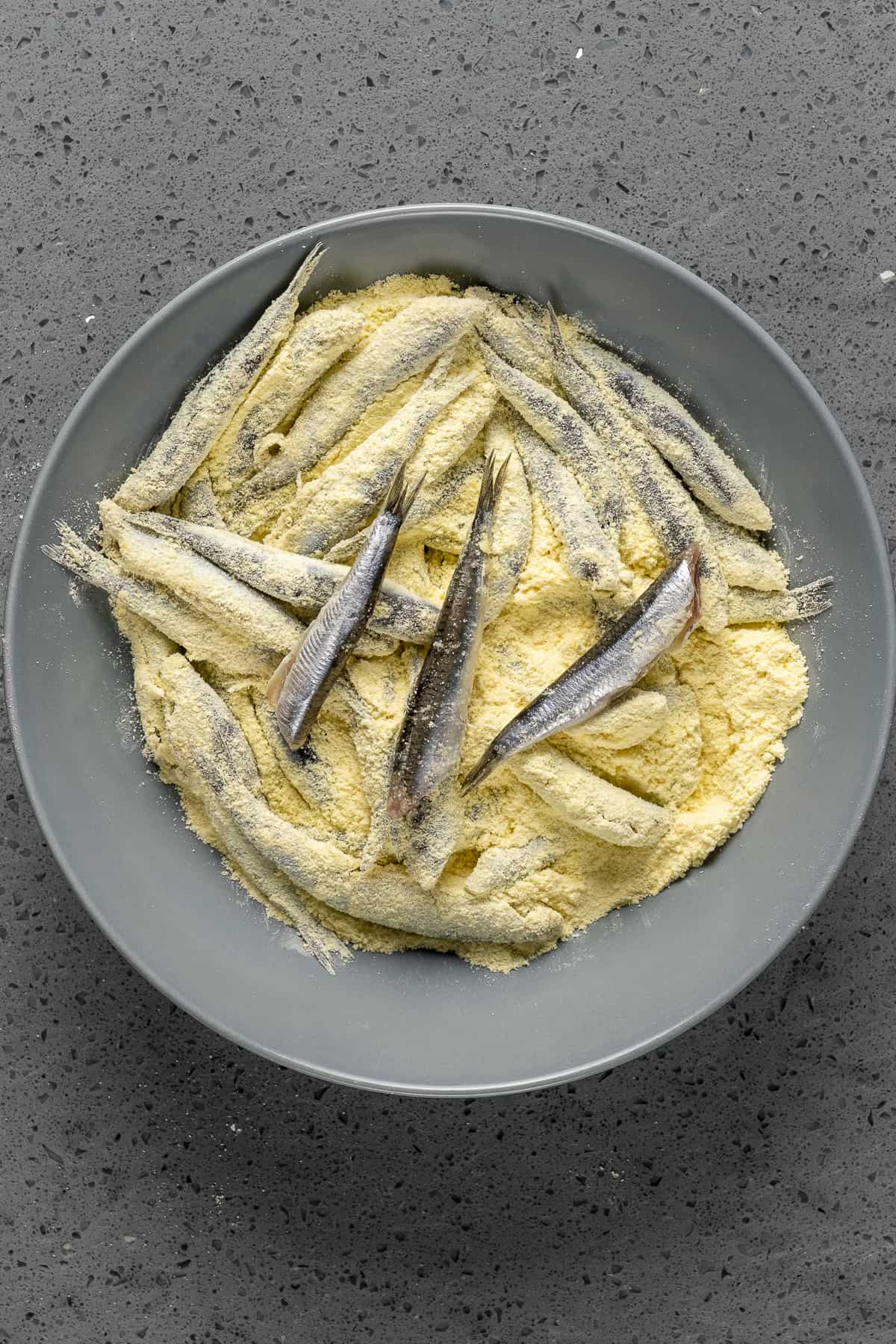 Fresh anchovies coated with cornmeal in a bowl.