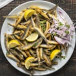 Fried fresh anchovies with lemon wedges and onion slices on a plate.