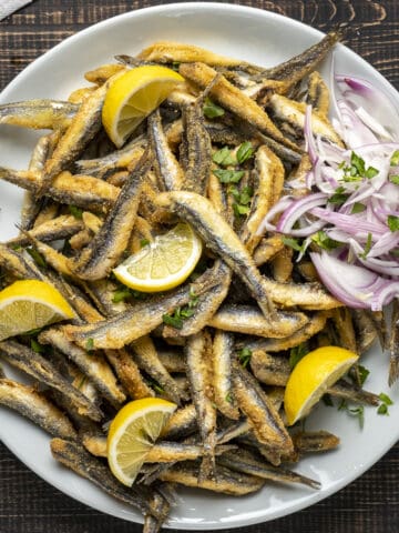 Fried fresh anchovies with lemon wedges and onion slices on a plate.
