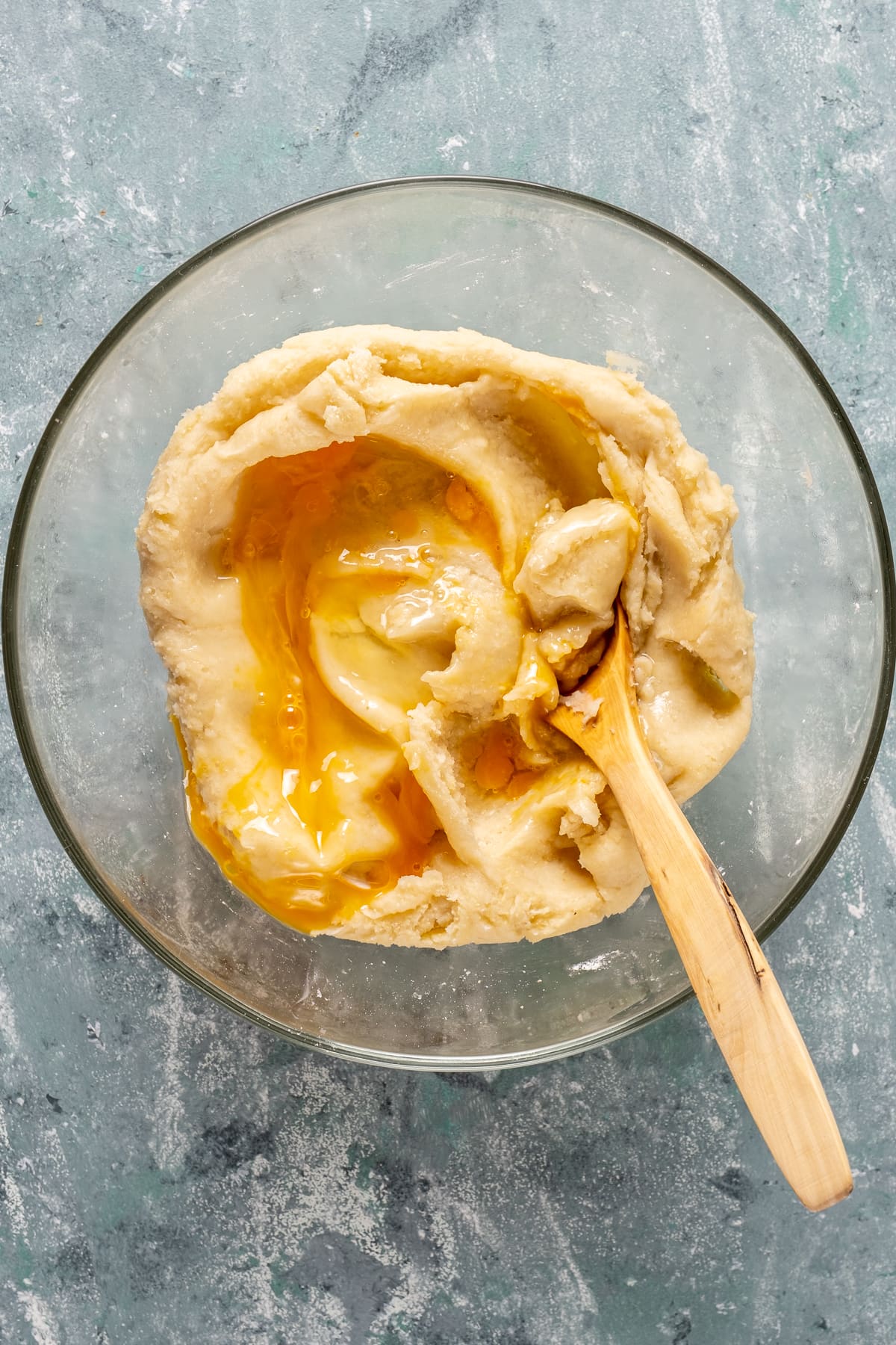 Eggs added in the tulumba batter in a mixing bowl and a wooden spoon inside it.