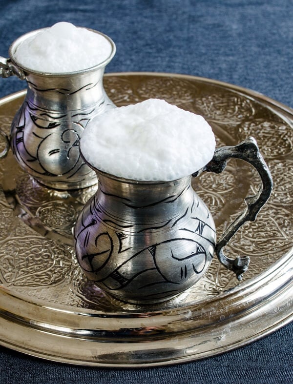 Turkish yogurt drink ayran photographed in two traditional copper cups on a copper plate.