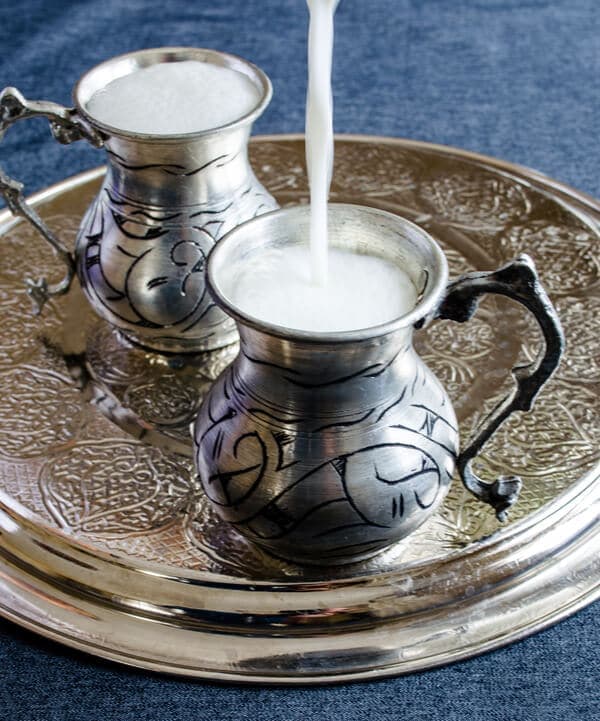 Turkish yogurt drink ayran photographed in two traditional copper cups on a copper plate.