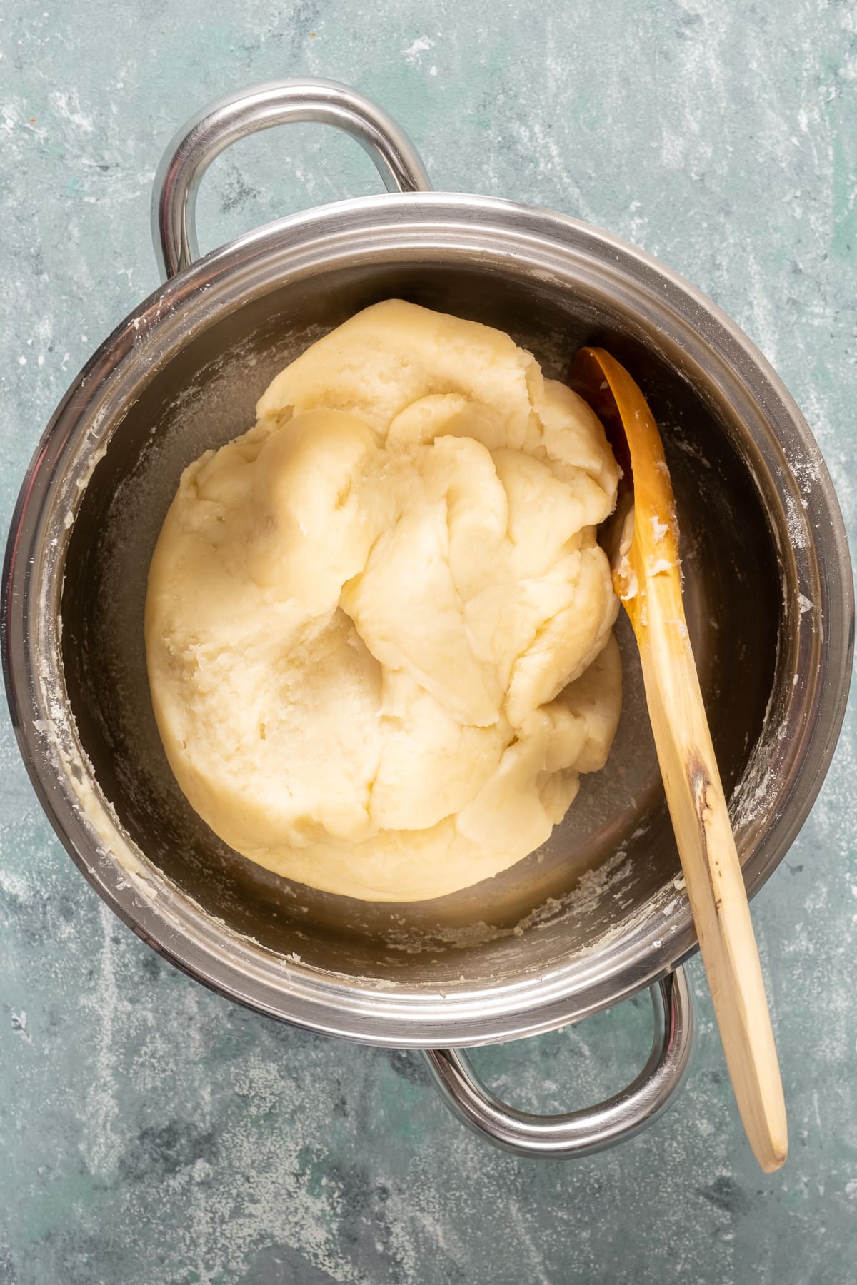 Tulumba dough in a pan with a wooden spoon inside.