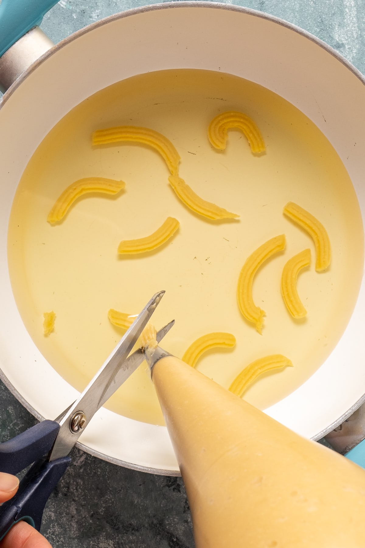 A hand cutting the squeezed batter from a piping bag