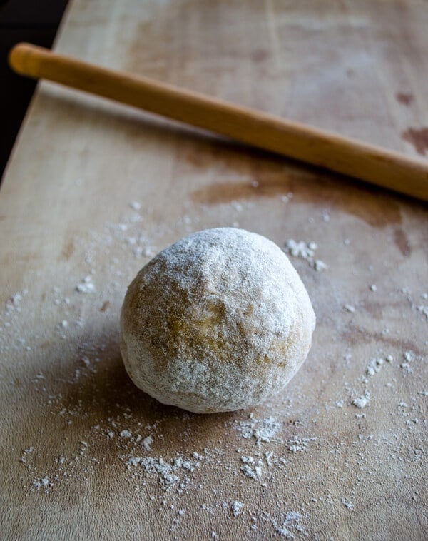 Turkish dumplings dough on a wooden board and a thin rolling pin on the side.