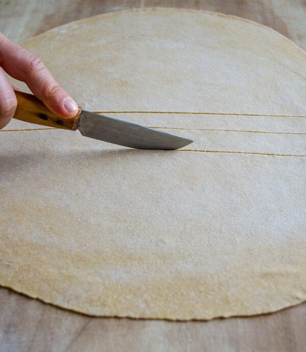 A hand cutting thin dough into tiny squares with a knife.
