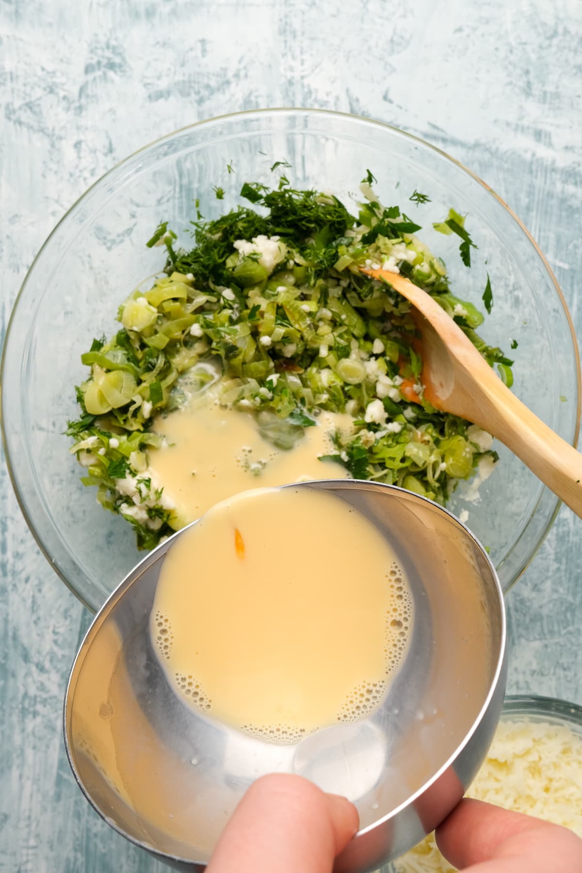 Pouring whisked egg and cream into the filling mixture in a glass bowl.