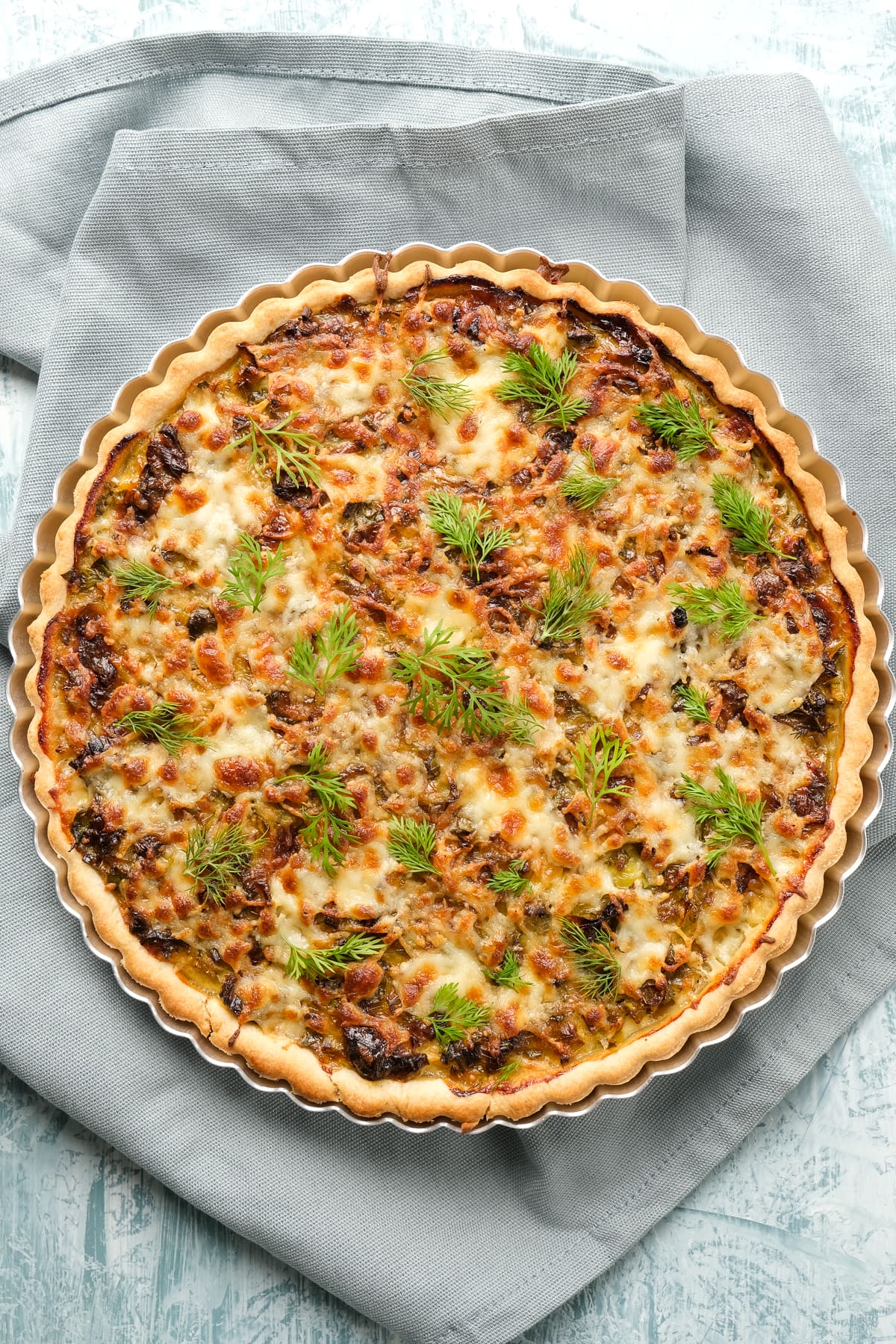 Quiche with cheese and leeks in a tart pan on a grey background.