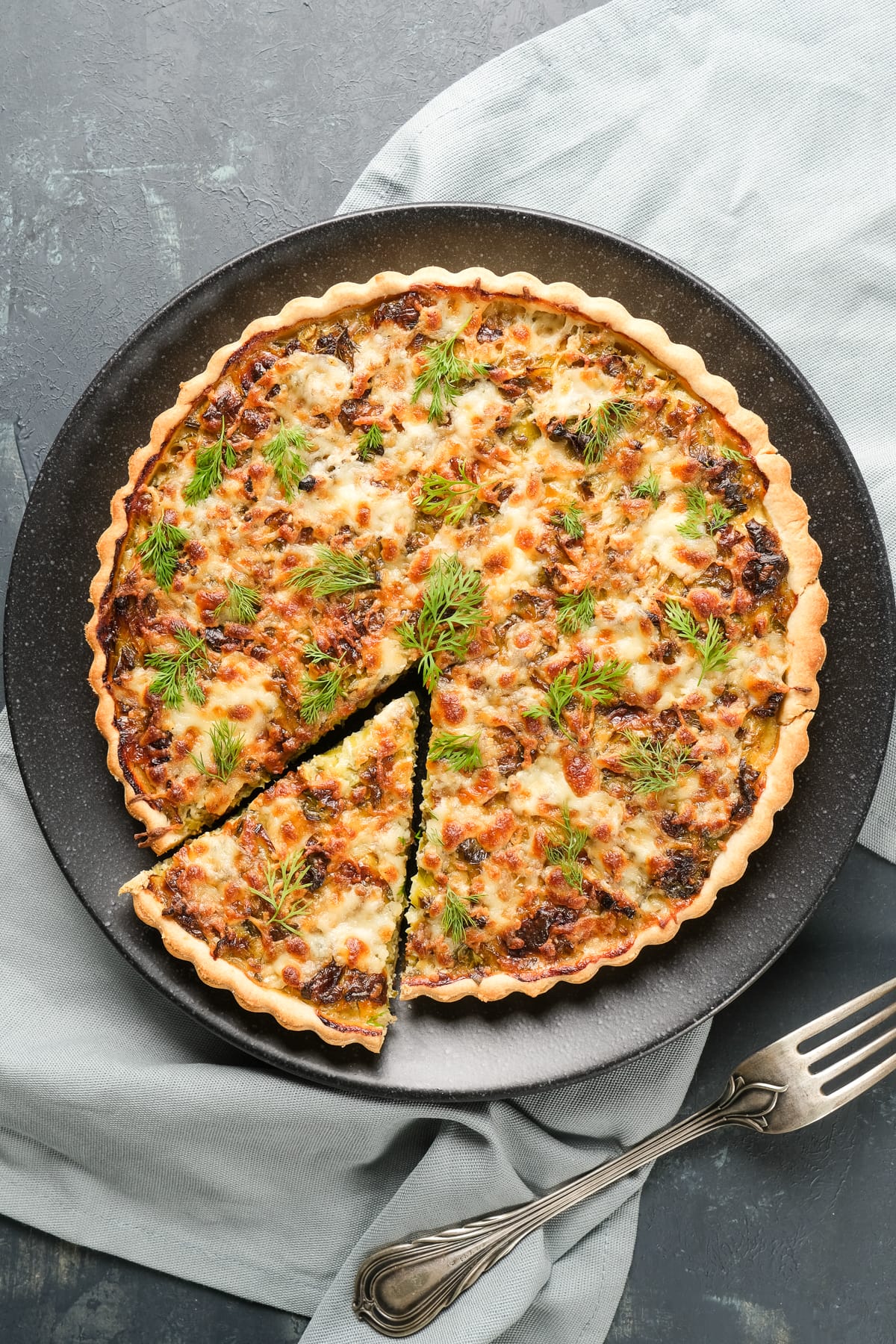 Leek quiche on a black plate, one slice is a bit apart.