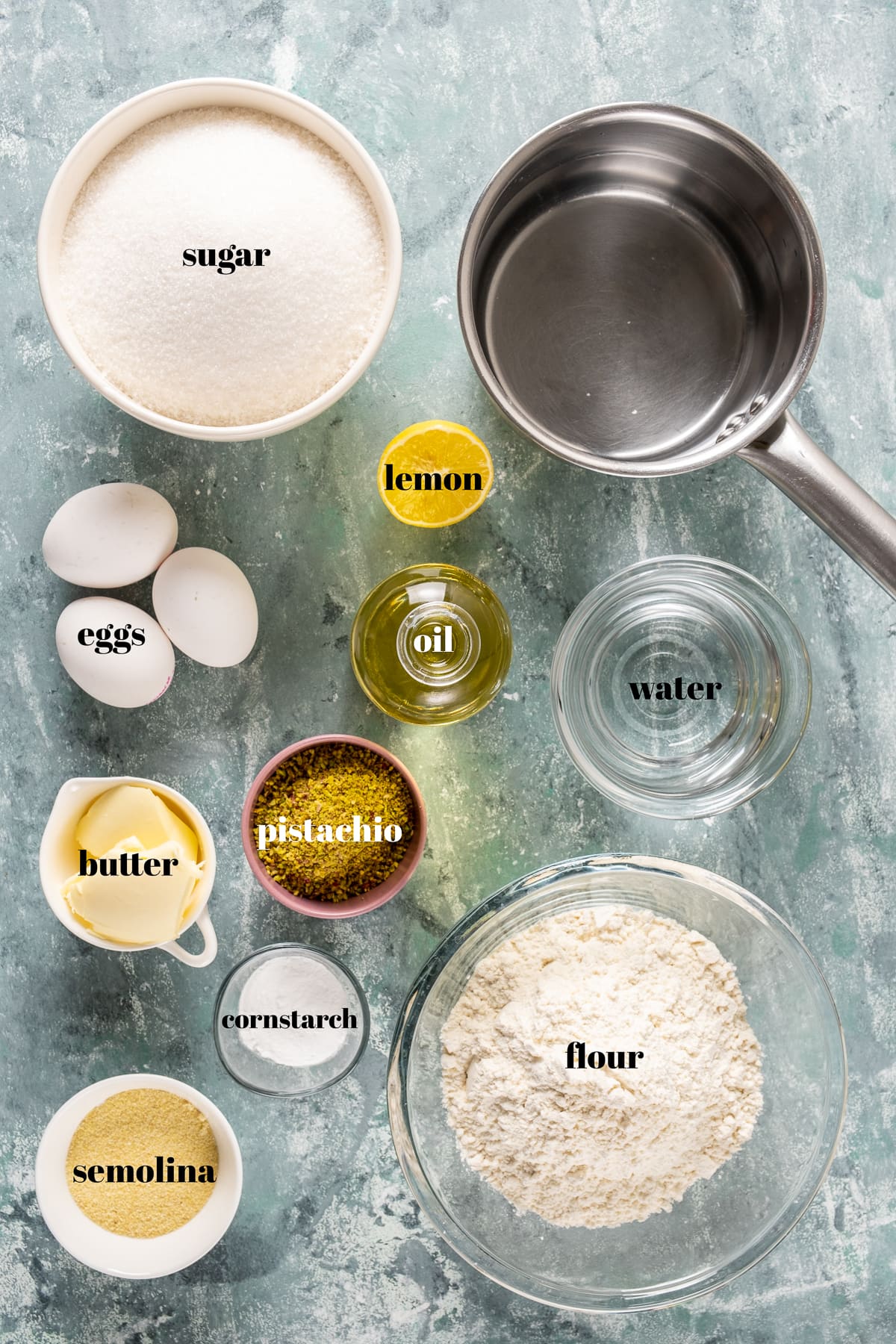 Flour, sugar, semolina, eggs, oil, pistachios, butter, lemon, cornstarch photographed on a light background.