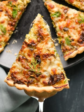 A slice of vegetarian quiche on a spatula, the rest is on a black plate on a dark background.