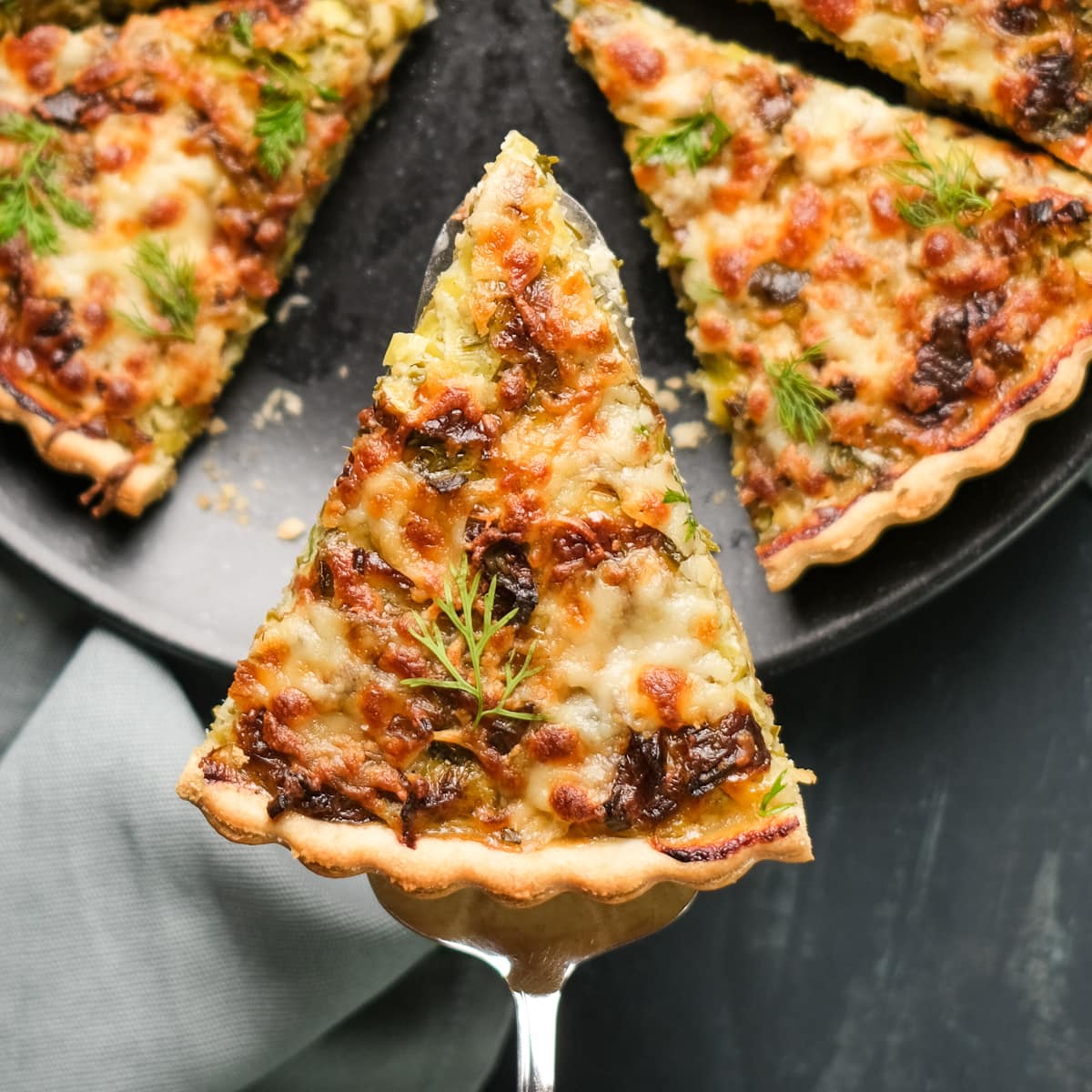 A slice of vegetarian quiche on a spatula, the rest is on a black plate on a dark background.