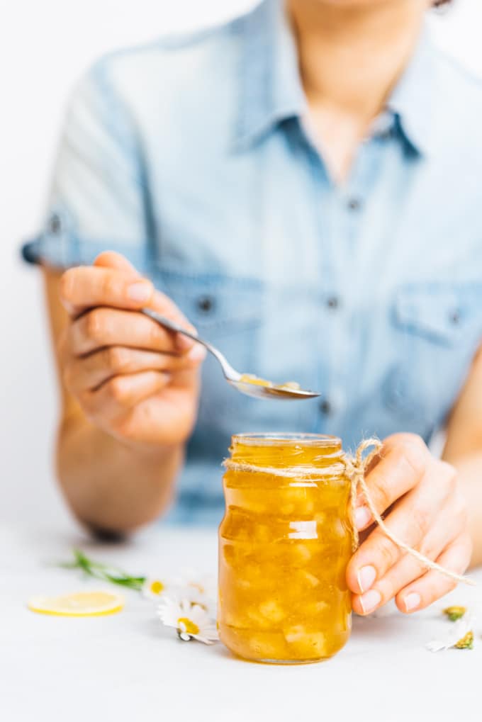 Woman with a blue shirt taking a spoon of lemon jam from a jar