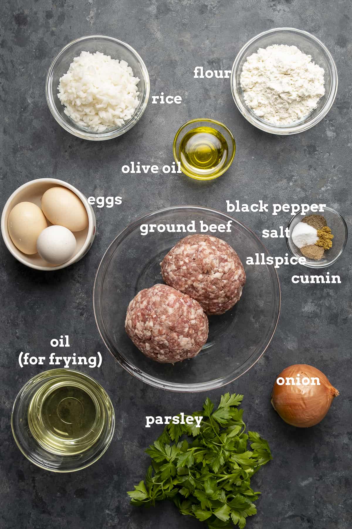 Ground beef, rice, flour, oil, onion, eggs, parsley, spices on a dark background.