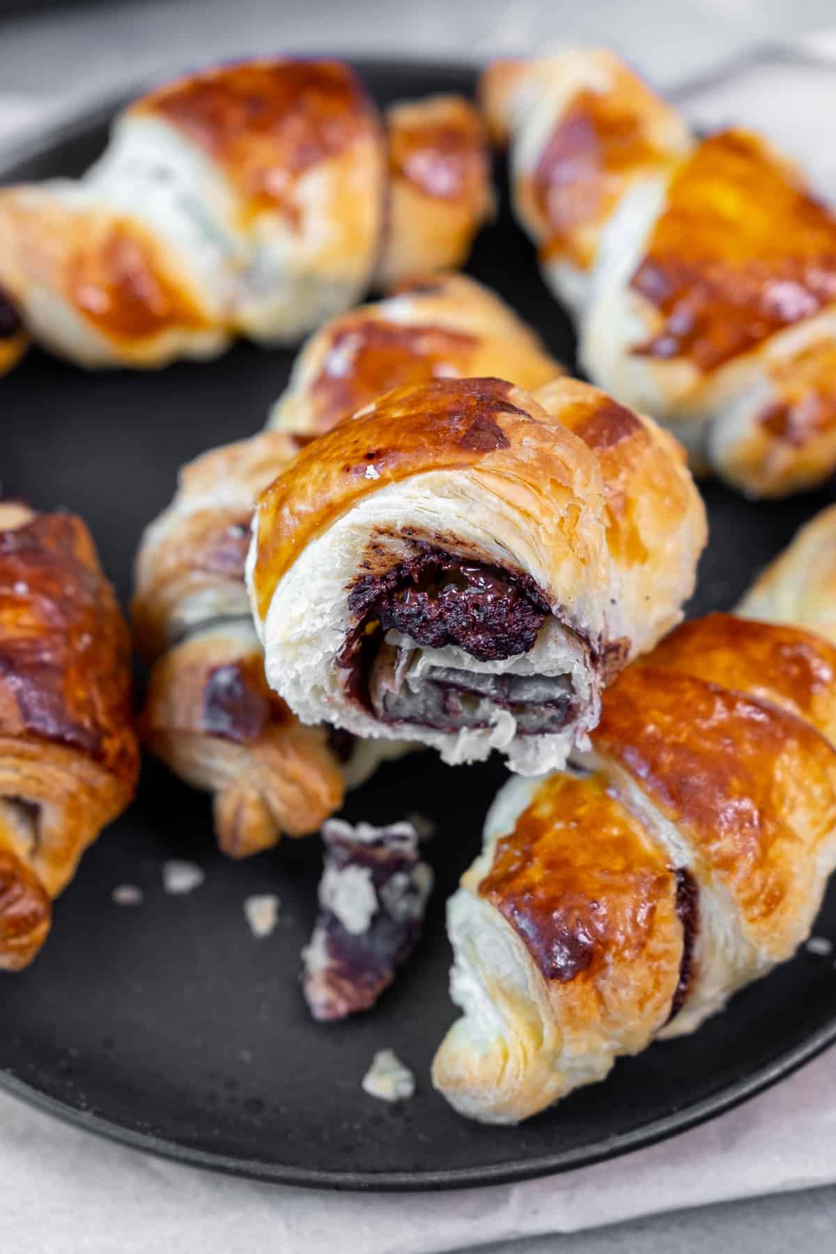 Chocolate filled puff pastry rolls on a black plate. The chocolate filling inside is shown.
