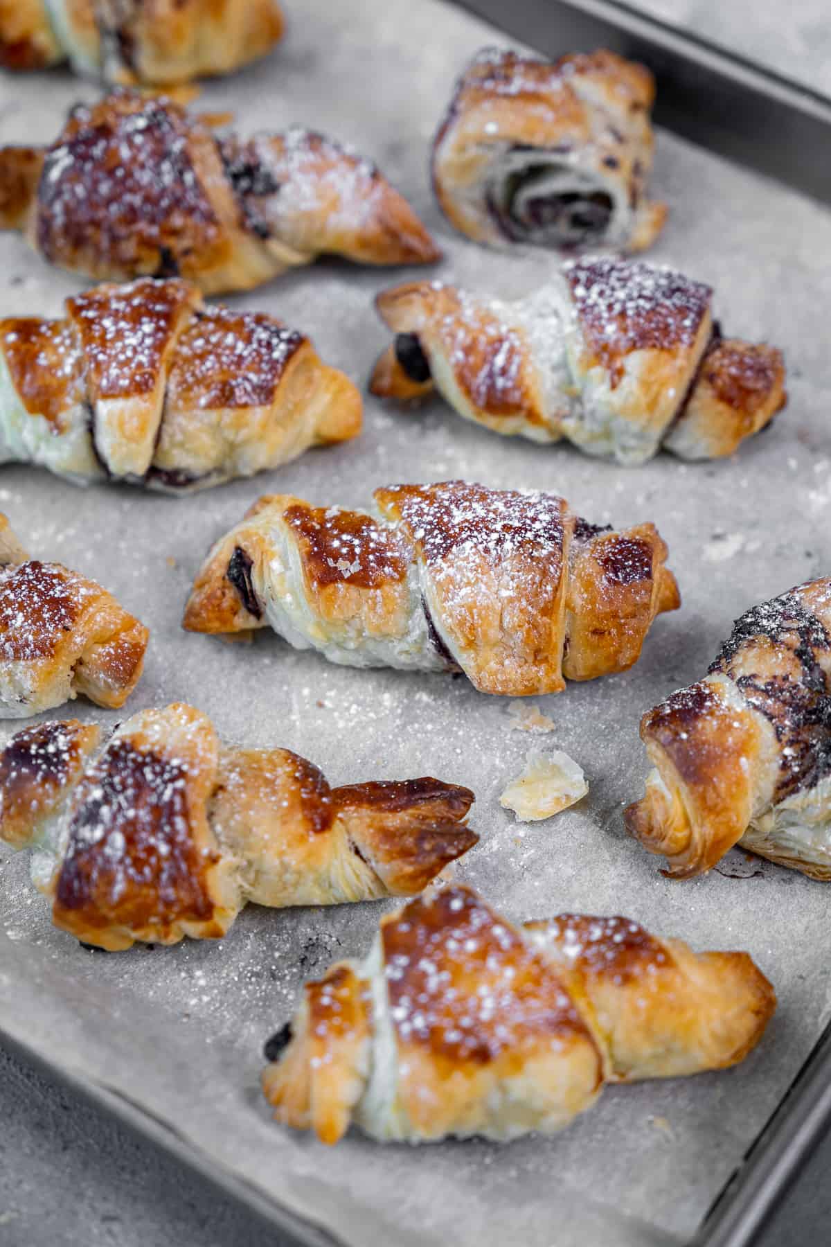 Puff pastries dusted with powdered sugar on a baking sheet.