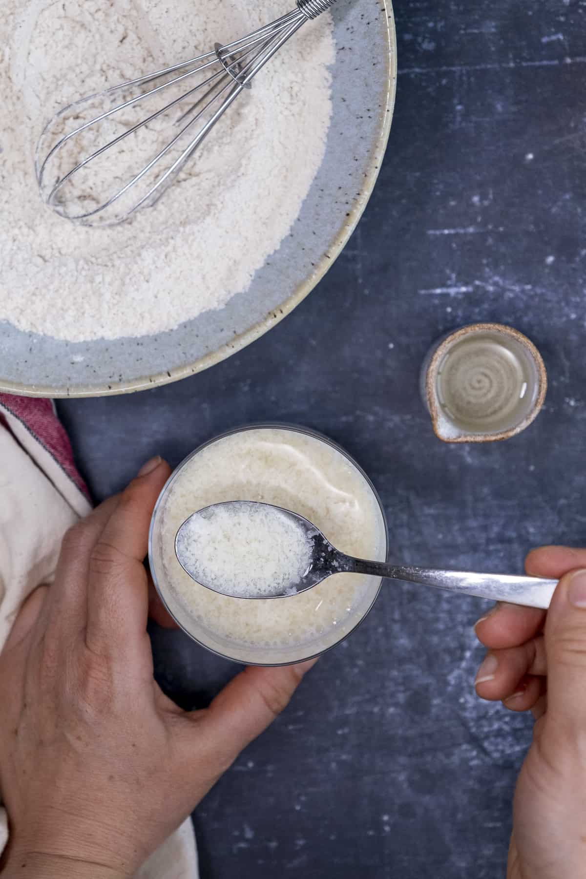 Hands mixing vinegar and almond milk in a glass with a spoon.