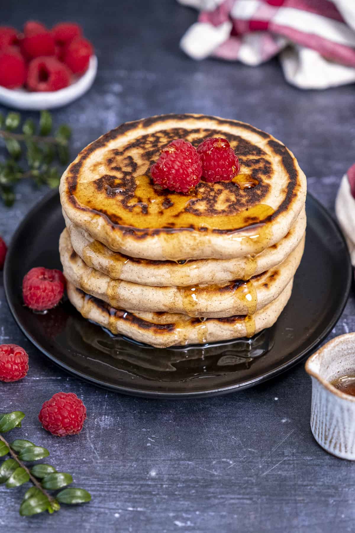 Pancakes topped with raspberries and drizzled with maple syrup on a black plate.