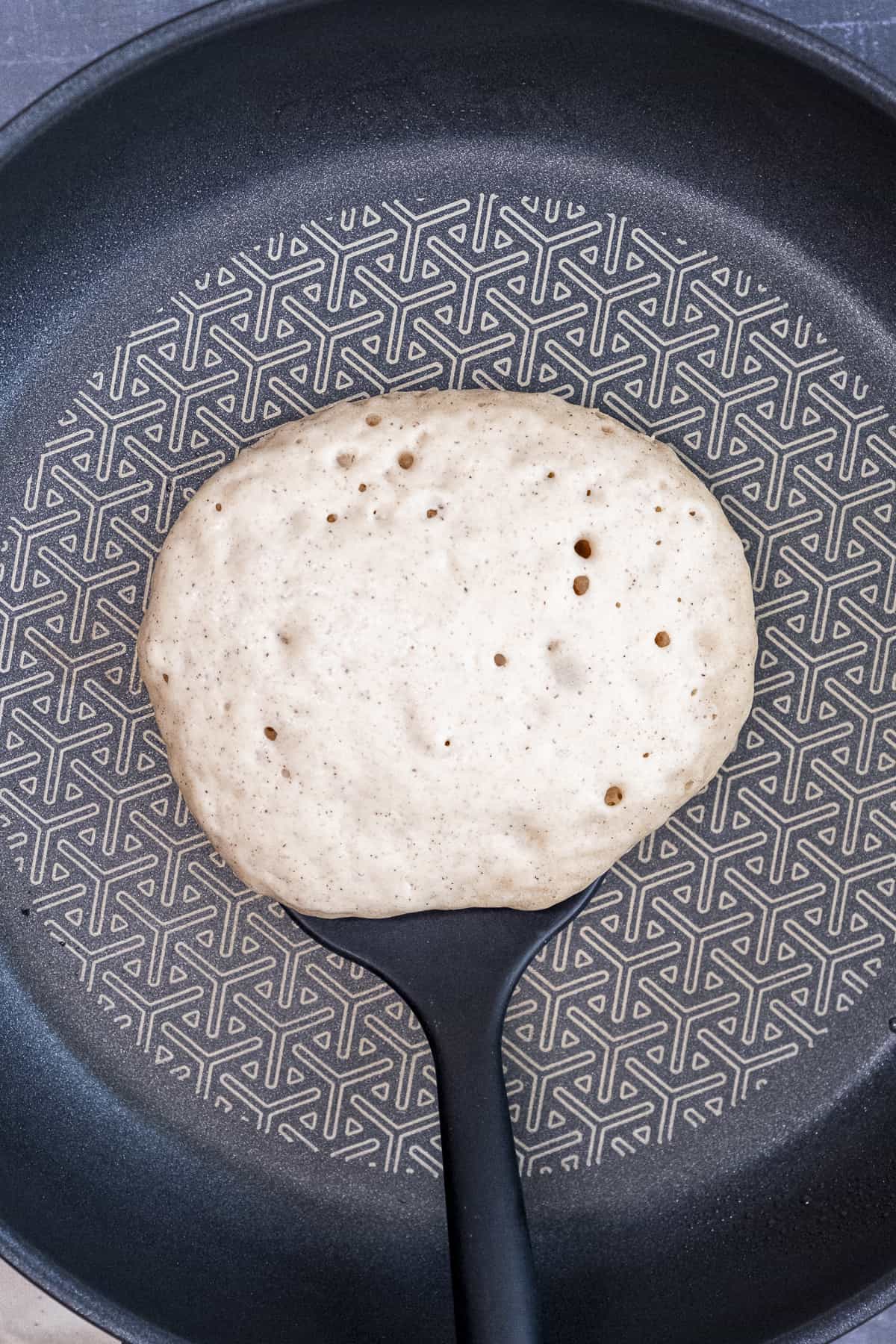 A spatula about to flip a pancake in a non-stick pancake.