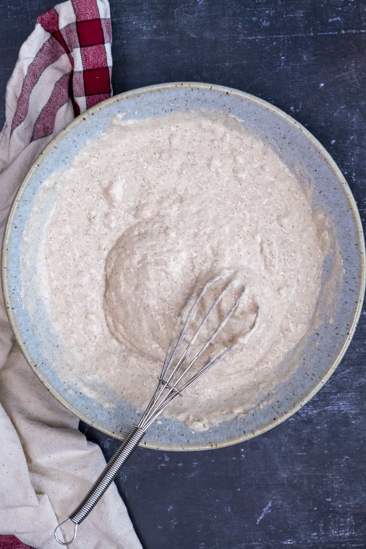 Pancake batter in a blue bowl and a hand whisk in it.