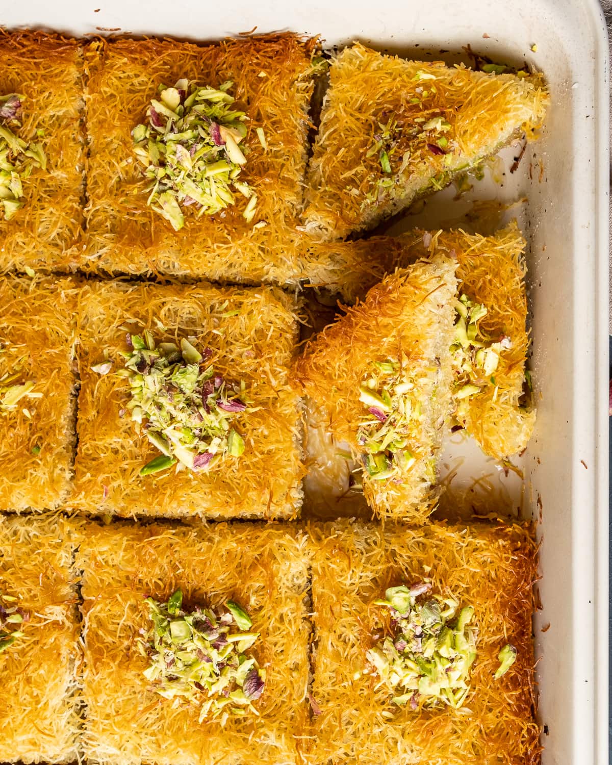 Baked golden top kadaif slices topped with crumbled pistachios in a pan.