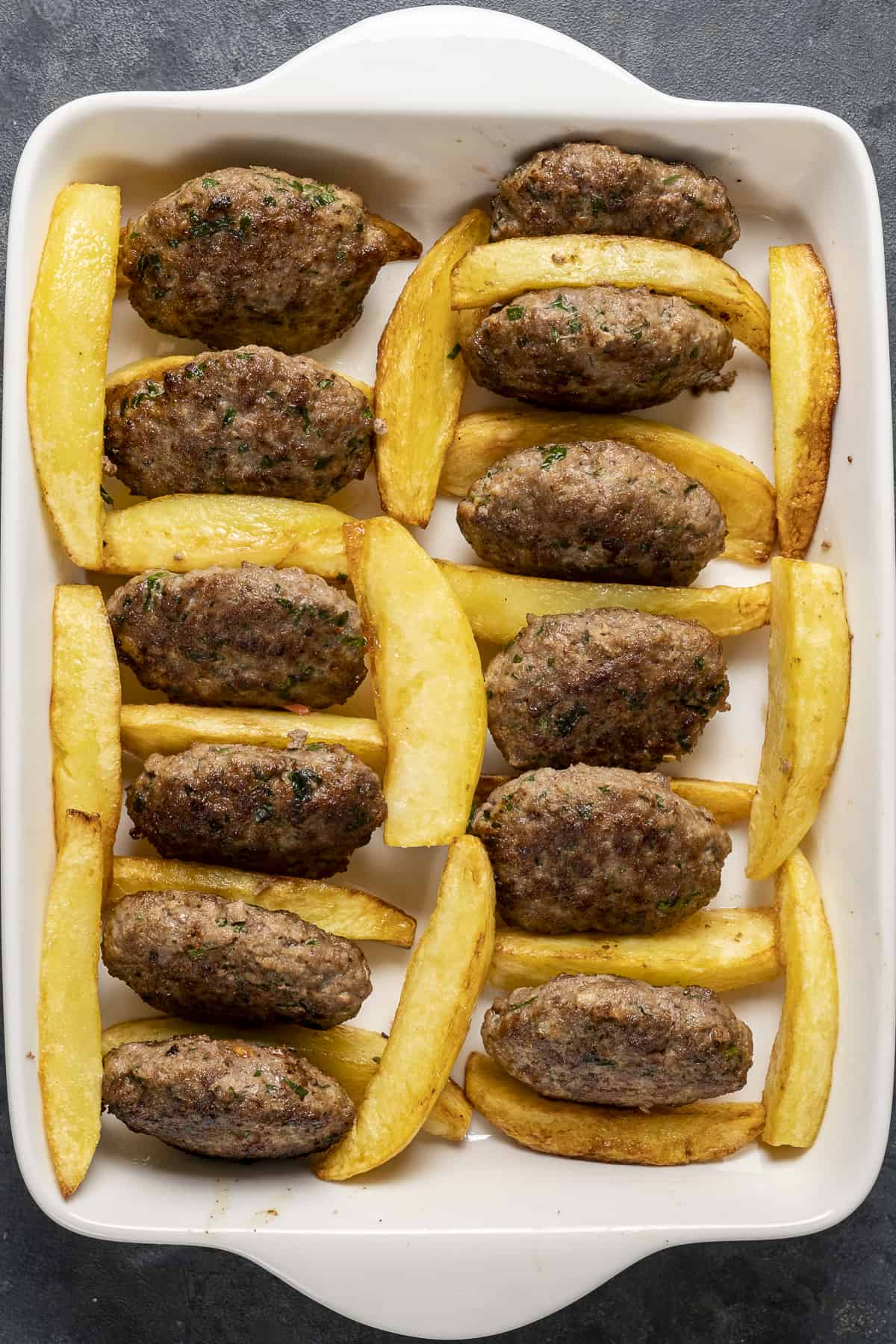 Fried potatoes and meatballs in a white baking pan.