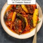 Baked meatballs and potatoes in tomato sauce served in a white bowl and a spoon on the side.