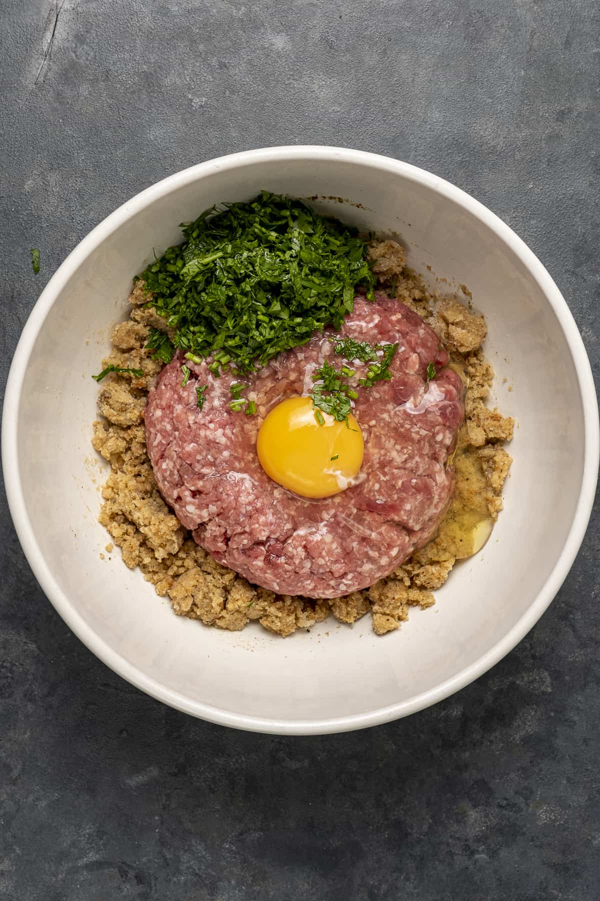 Meatball mixture with egg in a white bowl.