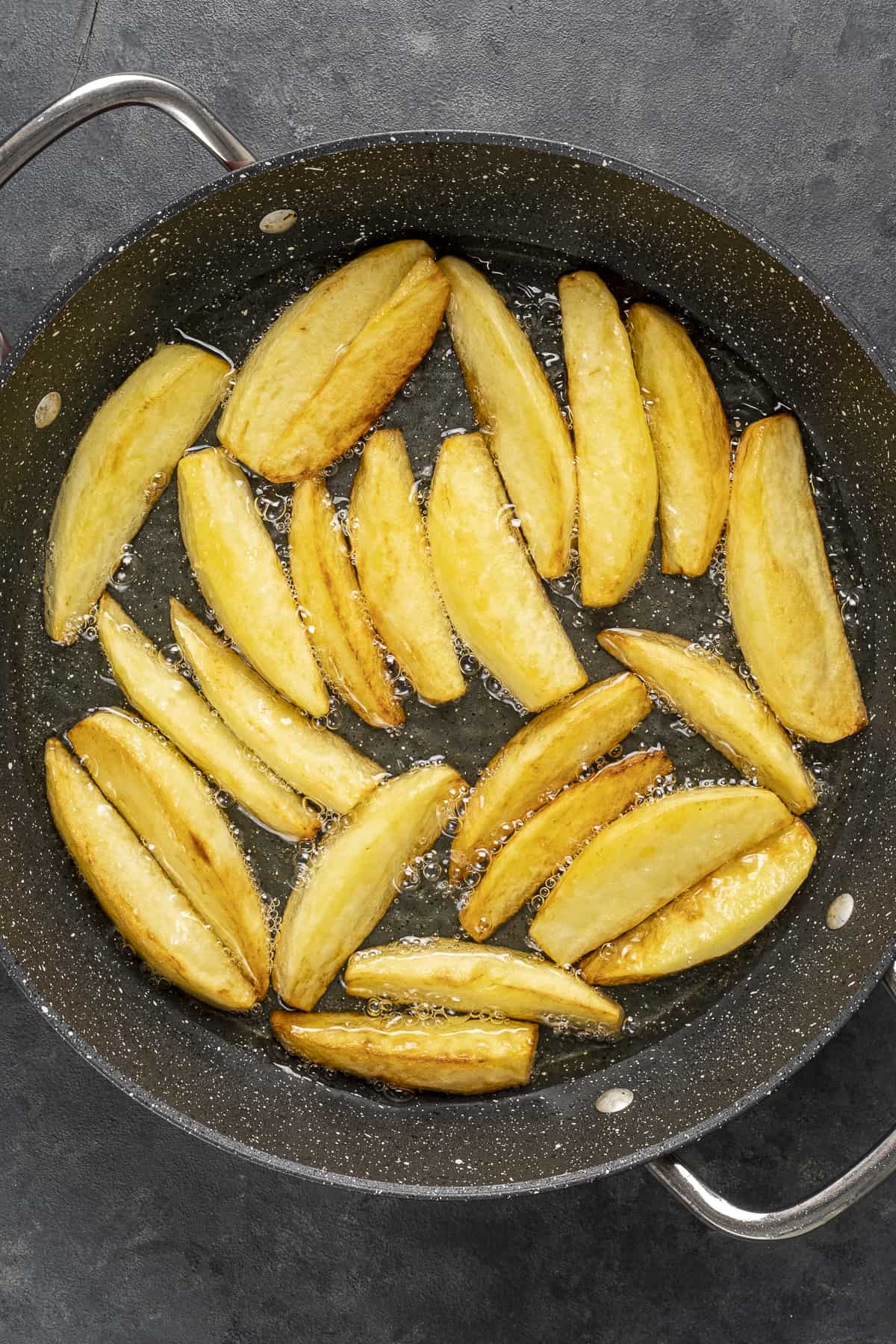 Potato slices frying in a pan.