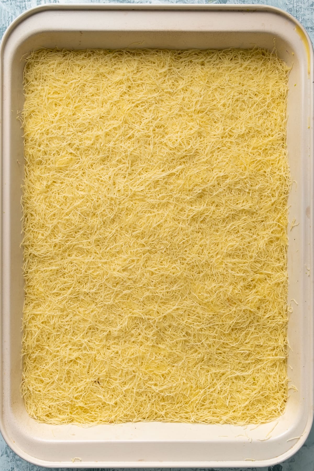 Raw kadayif ready to be baked in a rectangular pan.