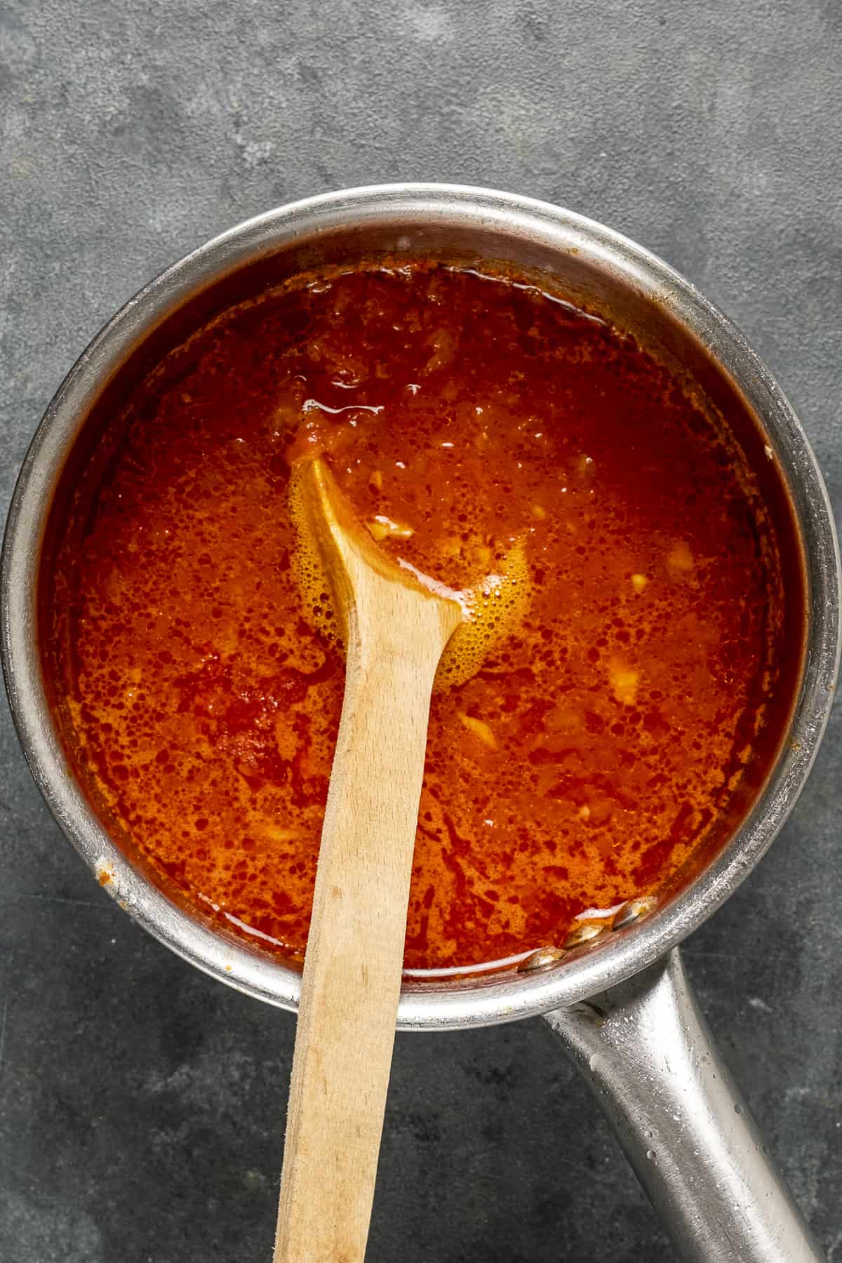 Tomato sauce in a saucepan and a wooden spoon inside it.