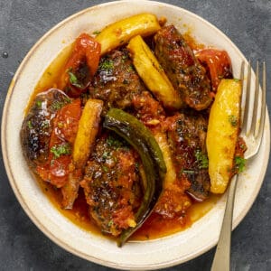 izmir kofte in tomato sauce served on a white plate and a fork inside it.
