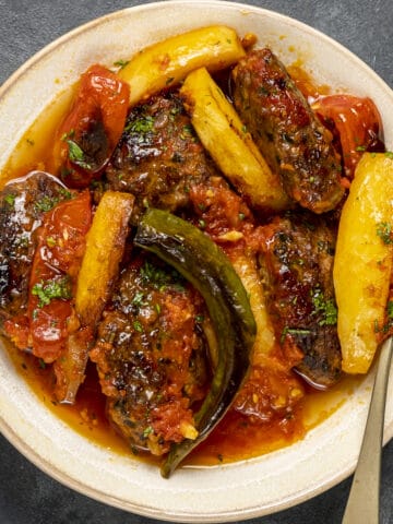 izmir kofte in tomato sauce served on a white plate and a fork inside it.