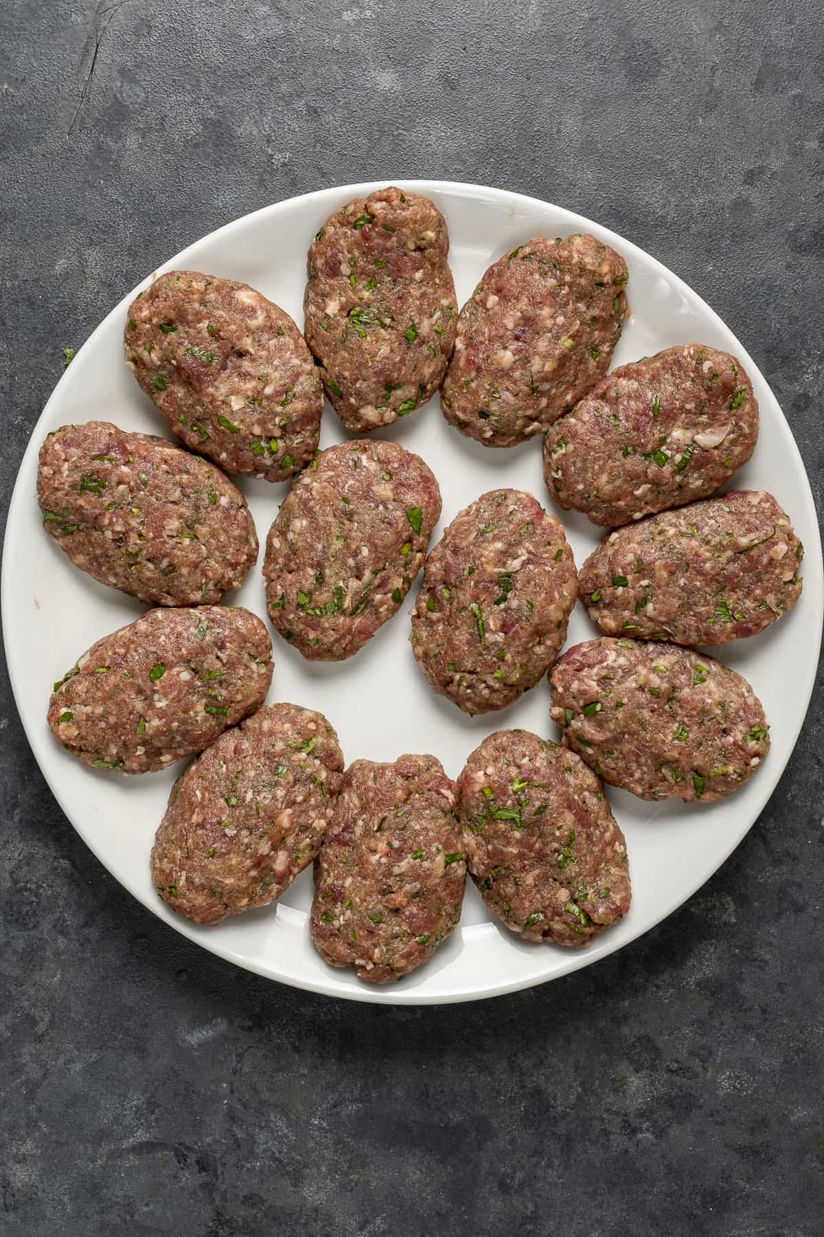 Uncooked oval-shaped meatballs on a white plate.